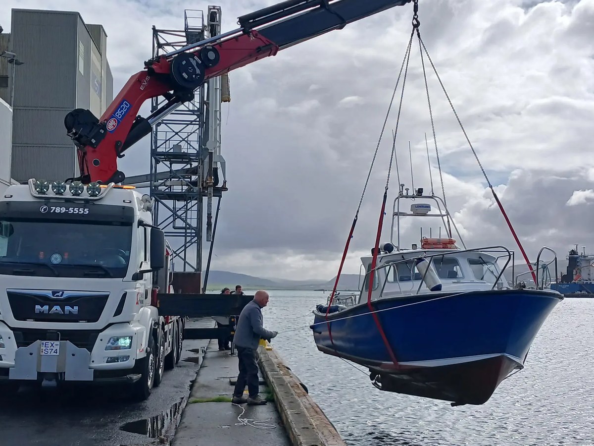 Kranabíll Þróttar hífir bláan bát við höfnina